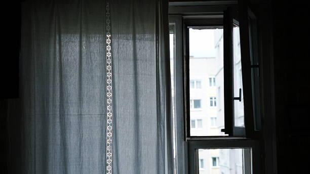 istock Small wooden window leaf is open in dark room with white curtain 1415072727