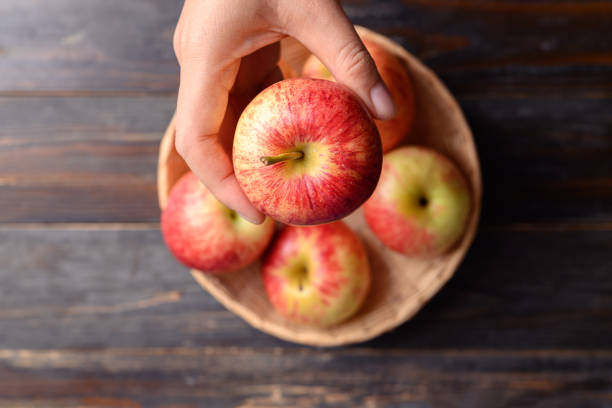 istock Red apple fruit in basket with hand on wooden background 1415081302