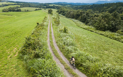 Mid age Japanese woman riding mountain bike down along a wide open country grassy field.