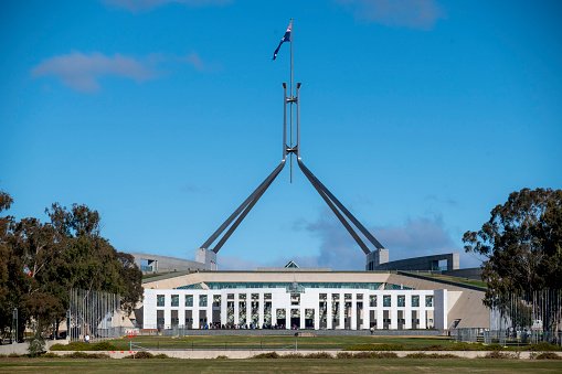 Building of Parliament on Capitol hill in Canberra - facade, entrance and columns illuminated with tall mast and flagpole on the roof. This is a public building free for admission by general public, belongs to people off Australia.