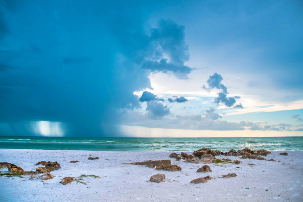 Travel to a tropical beach paradise along the seashore. Lush landscape, rock outcroppings, storm clouds gathering in the sunset sunrise horizon, dusk to dawn sky, Siesta Key Beach, Florida, Sarasota County. Tropical beach paradise with shades of blue, turquoise, white sands, and gathering tropical storm clouds in the distant horizon. Sunrise, sunset, dusk, dawn. Beautiful water lifestyle scene. Siesta Key, Florida. calm before the storm stock pictures, royalty-free photos & images