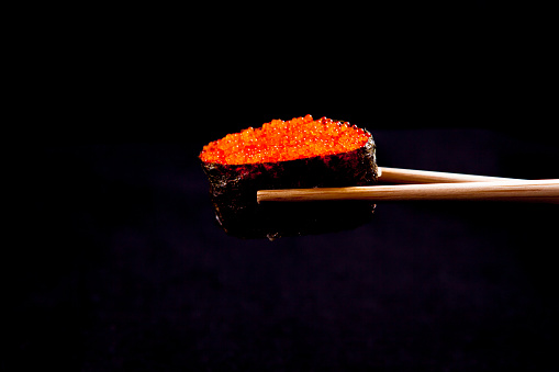A Tobiko Roe Sushi being held by wooden chopsticks
