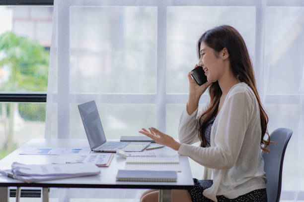 Asian businesswoman using smartphone to do accounting work with laptop and graph of financial reports in office Asian businesswoman using smartphone to do accounting work with laptop and graph of financial reports in office smart phone telephone research tax stock pictures, royalty-free photos & images