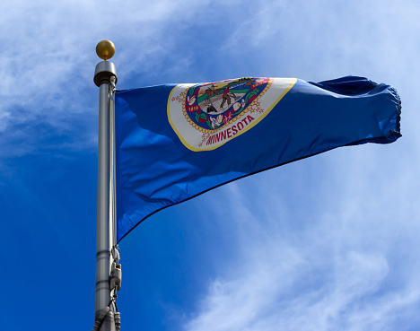 Close up outdoor view of a Minnesota state flag flying in the wind, with blue and white sky background.