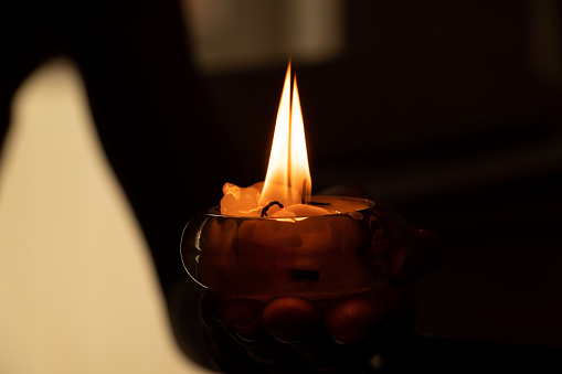 A woman's hand holds a burning candle in the dark, candle flame and religion, prayer and candle