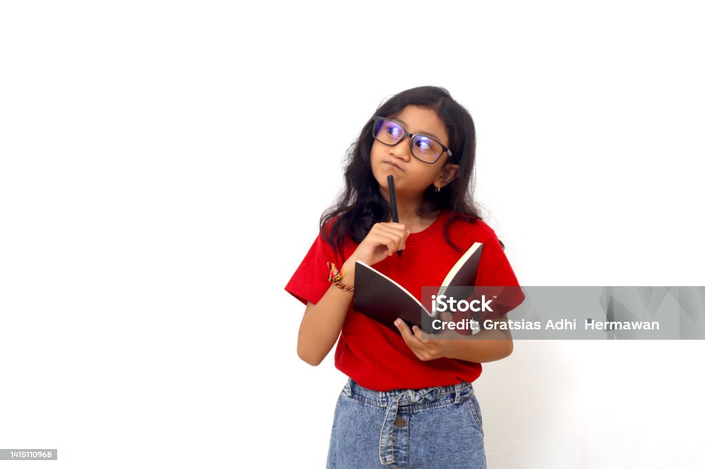 Thoughtful asian schoolgirl standing while holding a book and looking sideways. Isolated on white Child Stock Photo