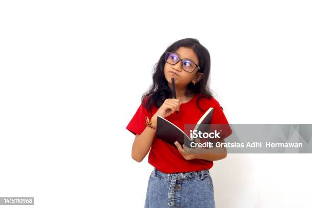 Thoughtful Asian Schoolgirl Standing While Holding A Book And Looking Sideways Isolated On White Stock Photo - Download Image Now
