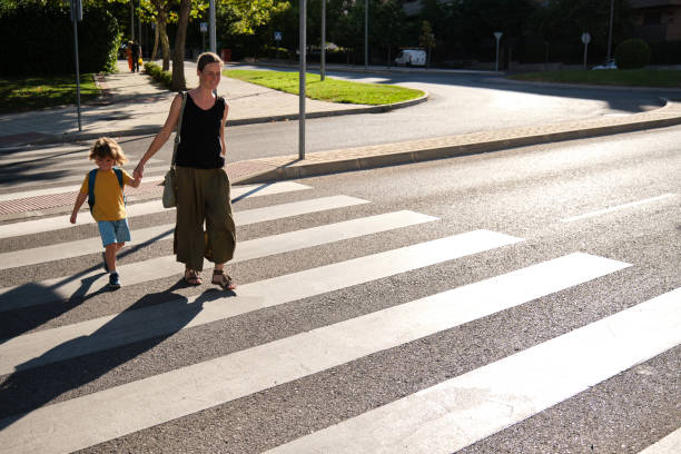 uma mãe e seu filho atravessando a estrada a caminho da escola - pedestrian - fotografias e filmes do acervo