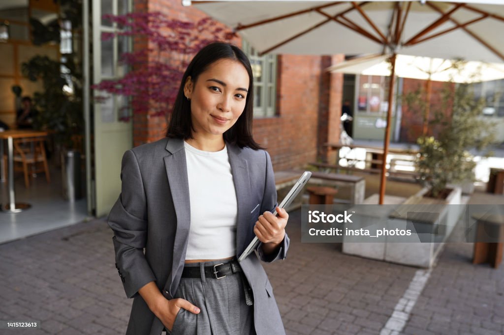 Young professional leader Asian woman manager wearing suit, outdoor portrait. Young elegant professional leader Asian woman, female executive retail manager supervisor, small business owner wearing suit holding digital tablet standing outdoor looking at camera, portrait. Human Resources Stock Photo