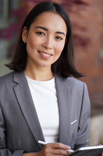 Confident young elegant successful professional leader Asian business woman, female hr, korean businesswoman manager wearing suit holding digital tablet looking at camera, vertical headshot portrait.