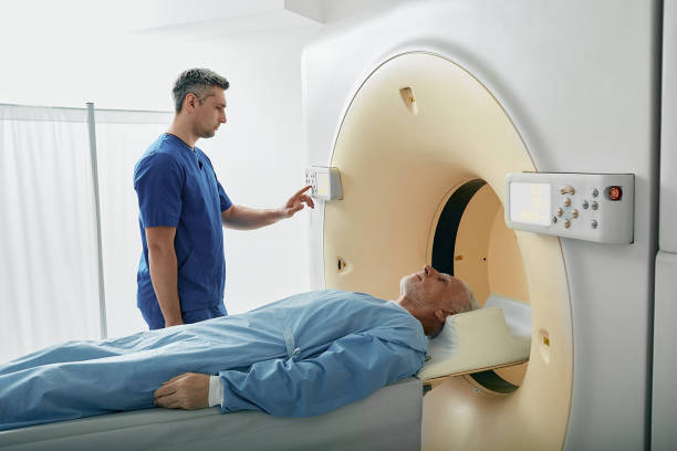 istock Radiographer operating computed tomography scanner being used to scan lying patient in radiology department of hospital. CT scanner 1415127407