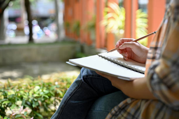 istock A hipster female noting her creative ideas in a notebook while sitting in the city park. 1415131121