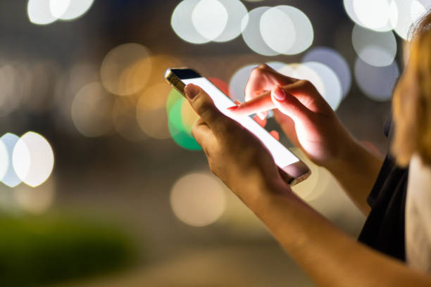 istock Woman hands using her mobile phone, city skyline night light background 1415134017
