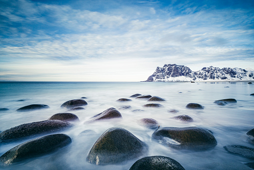 Utakleiv beach in the Lofoten archipel in Norway at the end of a beautiful winter day. Waves are flowing over the rocks in the foreground with snow covered mountains in the background. Long exposure image with smooth water.
