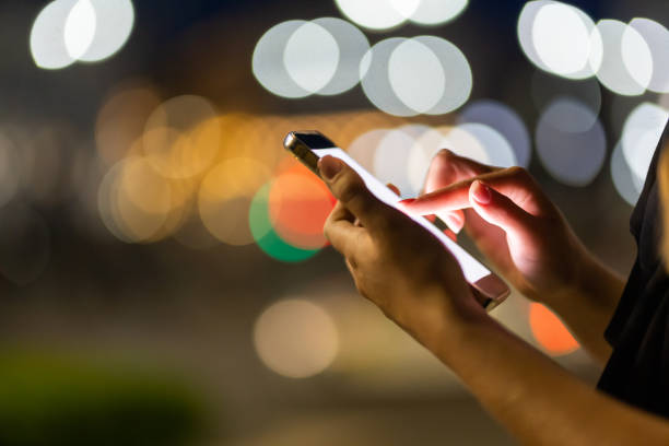 istock Woman hands using her mobile phone, city skyline night light background 1415134828