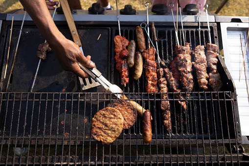 A close-up shot of an unrecognisable man cooking halal meat on a barbecue in a garden on a summers day in Northeastern England.
