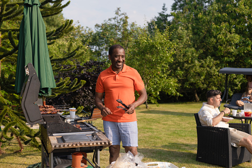 A shot of a senior man preparing a barbecue in his back garden on a bright summers day, all the meat on the barbecue is halal.
