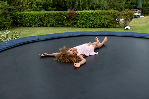 A shot of a young girl lying down after jumping up and down on a trampoline in the garden on a summers day, she is having fun.