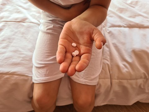 Child suffers from abdominal pain and holds medical pills. Treatment of diarrhea in children or healthy concept