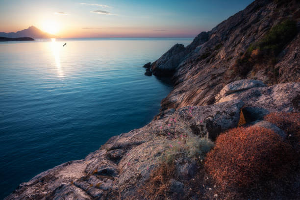 Sunrise at the sea coming up behind the sharp mountain glowing in the sea and the rocky coast