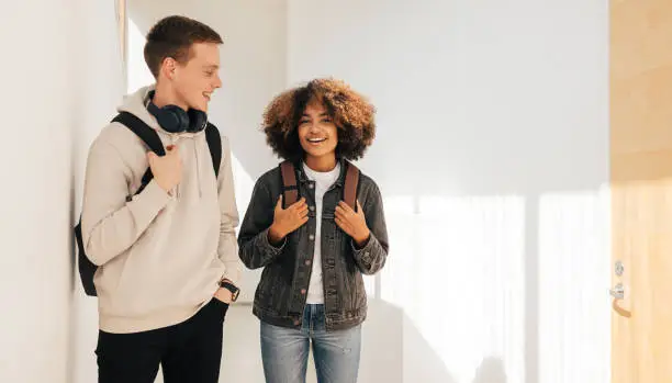 Photo of Smiling friends walking in college corridor. Classmates talking to each other.