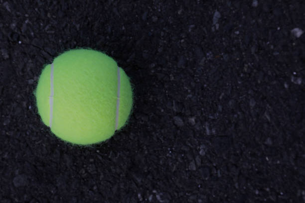 Tennis ball on the street, dark asphalt with rough surface, no people