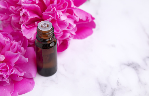 glass bottle with essential oil on marble background with peony flowers