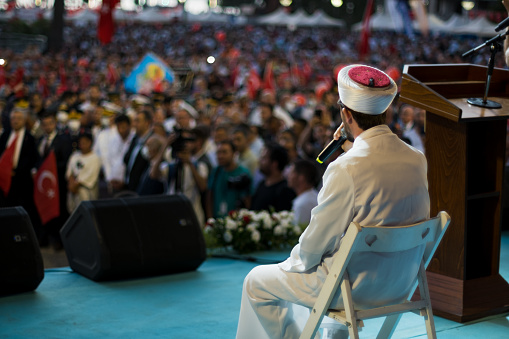 Izmir, Turkey - July 15, 2022: July 15 Day of Democracy in Turkey Izmir. Rear view of an imam with microphone on the stage and in front of the folks
