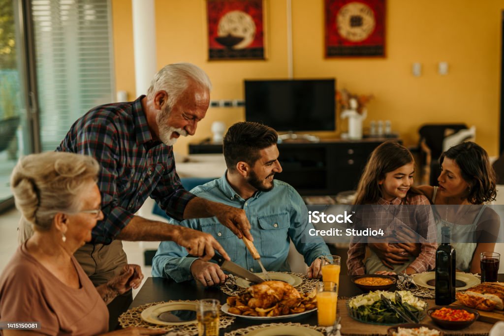 Thanksgiving family day Happy grandfather cutting turkey for his extended family on Thanksgiving or Christmas lunch. Domestic Life Stock Photo