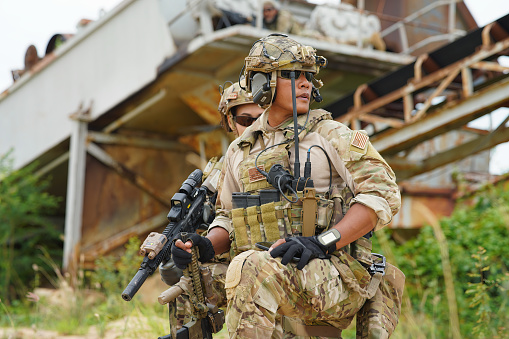 soldado en el campo de batalla sentado de rodillas en el suelo sostenga la alerta de arma mire a su alrededor photo