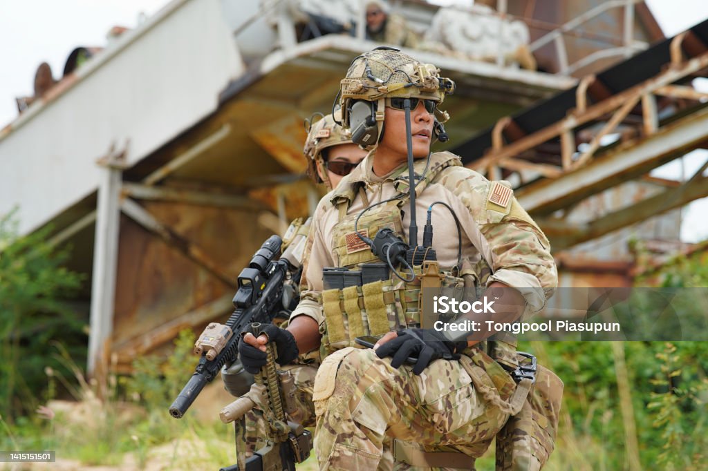 soldier in the battle field sitting knee down on the ground hold the gun alert look around 2 Army military soldier in the battle field sitting knee down on the ground hold the gun alert look around ready to fire weapon Militant Groups Stock Photo