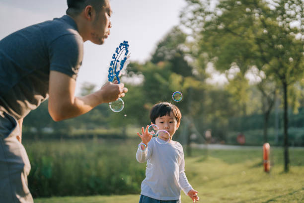 istock Asian chinese father playing with son at park blowing bubbles spending bonding time together 1415153419