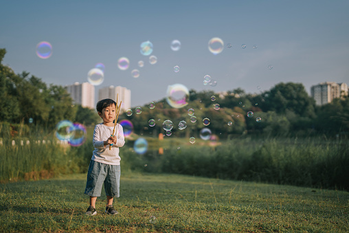 Asian chinese young boy blowing bubbles at public park enjoying playing