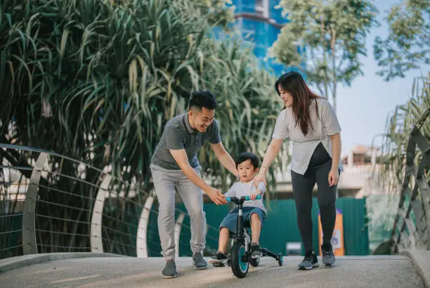 Photo of Asian Chinese boy learning cycling in public park with his 2 parents during weekend morning