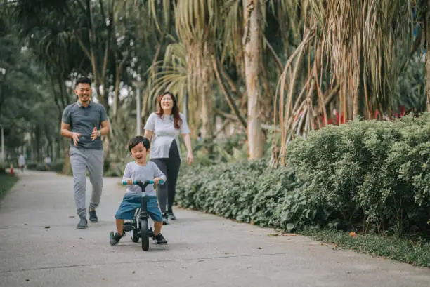 Photo of Asian Chinese boy learning cycling in public park with his 2 parents during weekend morning
