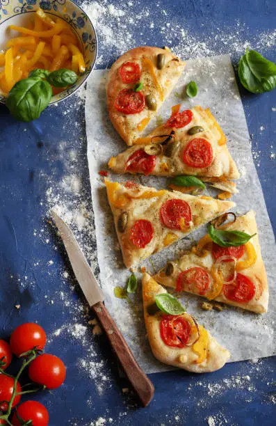 Homemade focaccia bread with fresh vegetables and basil leaves. Blue background. Directly above. Concept of Italian food.
