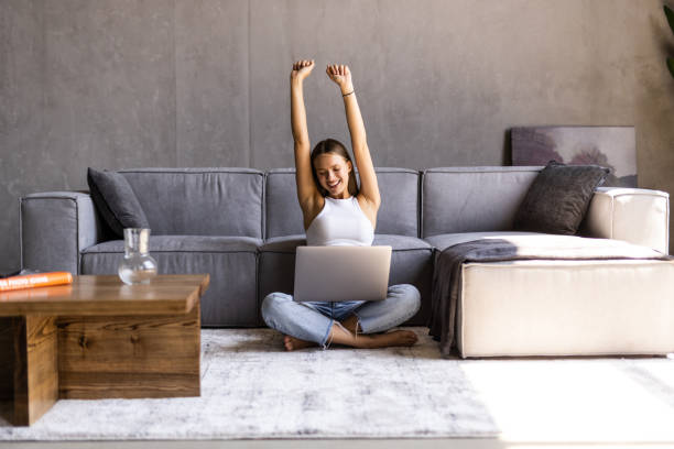istock Smiling young woman stretching her hands while sitting at a couch at home with laptop computer 1415162217