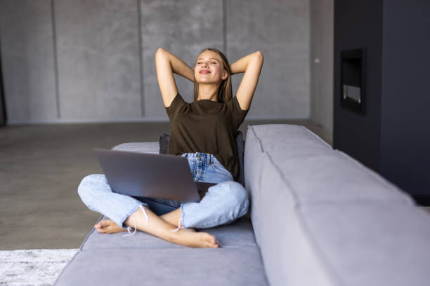 istock Young woman stretching her hands while sitting at a couch at home with laptop 1415162283