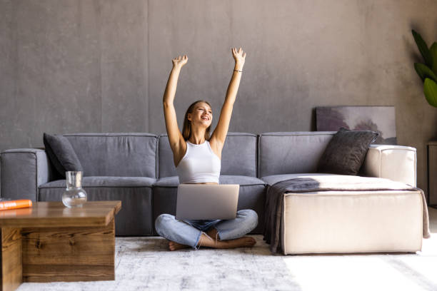 istock Pretty woman celebrating something while working with laptop sitting on a couch at home. 1415163526