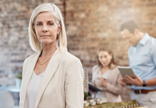 istock Serious, confident and executive professional or manager leading her busy team in planning. Mature urban developer standing as her employees design a model in an architecture firm in the background 1415165227