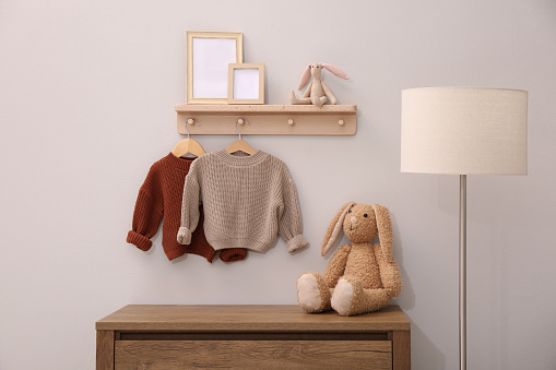 Children's room interior with stylish wooden furniture, baby clothes and lamp
