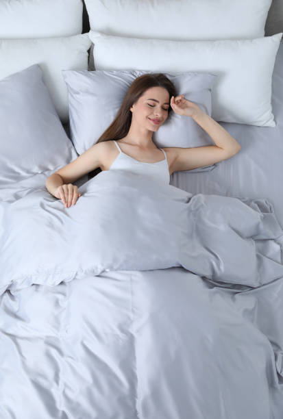istock Young woman awaking in comfortable bed with silky linens, above view 1415166845