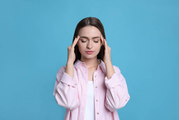 istock Young woman suffering from headache on light blue background 1415167050