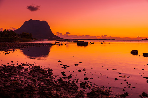 Quiet low tide ocean and warm sunset. Le Morn mountain in Mauritius.
