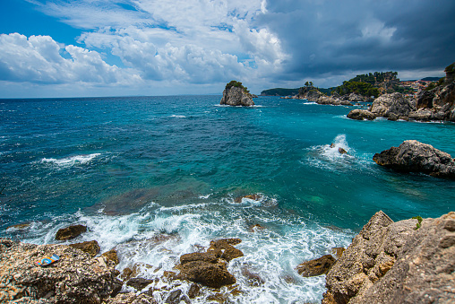 Exotic beach near Parga with big rock in the blue sea, in a pine trees forest. Background view of horizon and blue sky