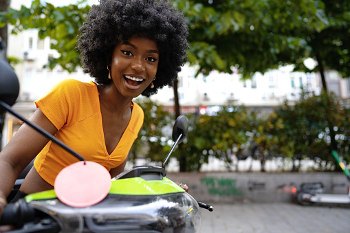 Portrait of young african american woman riding green motorbike in the city, close up