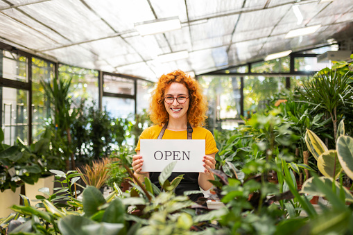 Young happy woman working in flower shop ,she is holding open sign
