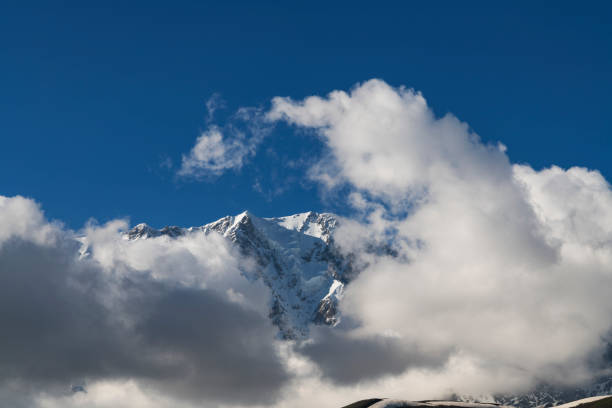 Clouds over the snow covered mountains. High mountains peak, winter landscape.