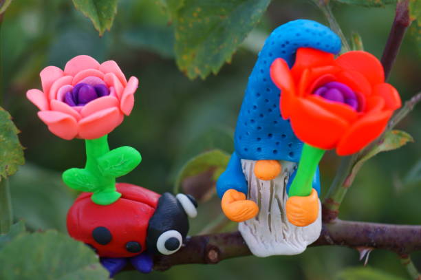 Figures of a dwarf and a ladybug with flowers on a tree branch. Fabulous toys made of plasticine.