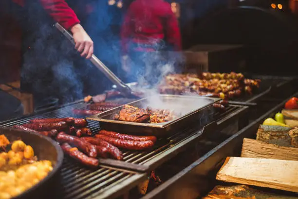 Photo of Outdoor street food festival. Chief cooking sausages, meat and potatoes cooking on an outdoor griddle